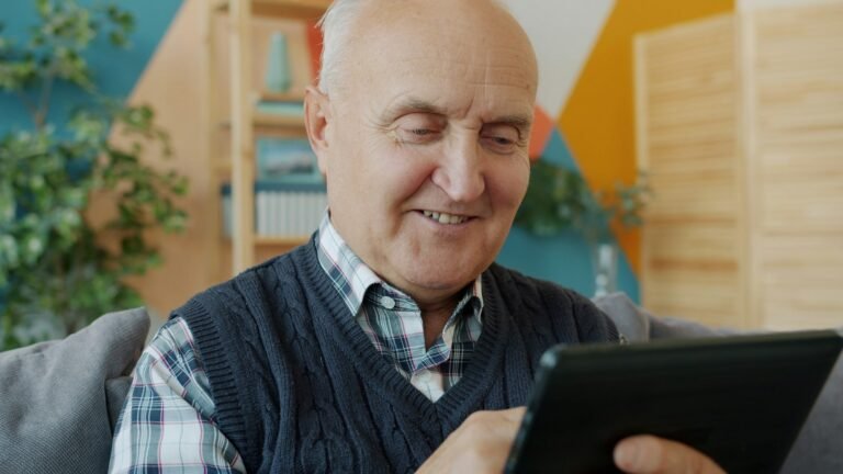 Homme âgé souriant utilisant une tablette chez lui